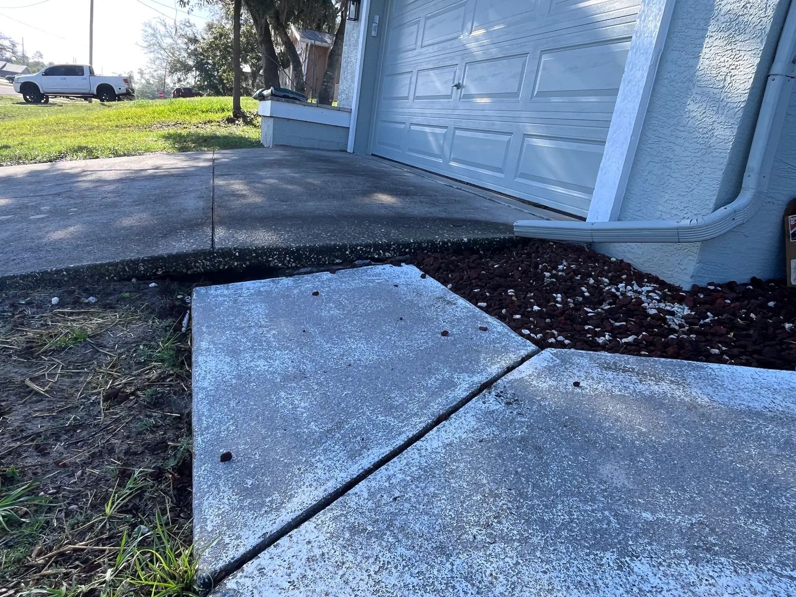 Uneven sidewalk panels creating a trip hazard beside a driveway