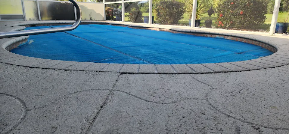 Cracked concrete pool deck beside a swimming pool showing visible surface damage