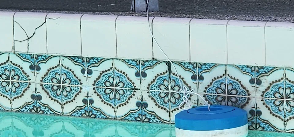 Cracked concrete pool coping along the edge of a swimming pool