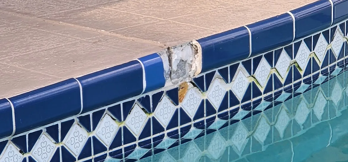 Missing and damaged blue swimming pool tile along the pool edge