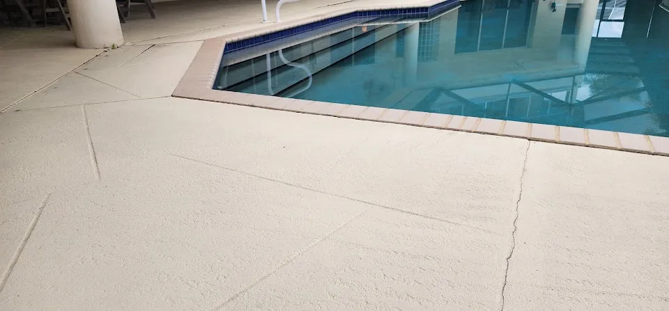Cracked concrete pool deck beside a swimming pool before concrete lifting and repair